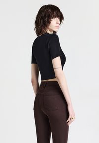 Top nero corto con maniche corte abbinato a jeans marroni a vita alta. L'outfit presenta un design aderente e una texture liscia.