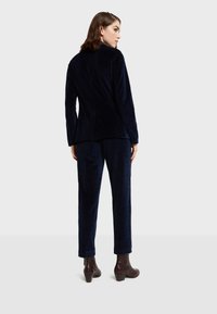 Námornícky modrý sametový oblek s upraveným sako a rovným strihom nohavíc, s výstrihom do "V", zadným rozventilovaním a textúrovanými akcentmi na látke.