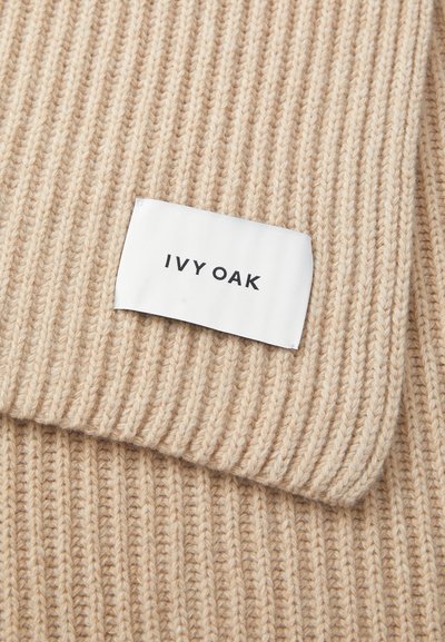 Beež ribaga kootud kangas, millel on selgelt nähtav valge silt, millele on kirjutatud "IVY OAK". Tekstuuriga pind, lähedalähenemine kangale ja silte.