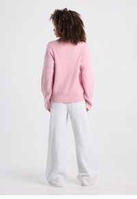 Maglione rosa a coste con spalle scese, abbinato a pantaloni della tuta grigi oversize. Tessuto morbido, vestibilità rilassata e dettagli di design minimalisti.