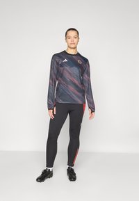Sportieve lange mouwen shirt in donkerblauw met een abstract patroon in rood en grijs, gecombineerd met zwarte leggings met rode accentstrepen en sportschoenen.