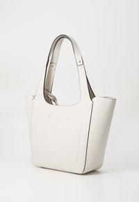 Sac fourre-tout blanc texturé avec des bords arrondis, bord noir, deux courtes poignées et des accents dorés subtils. Présente une poche avant.