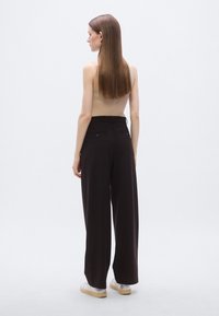 Pantalon marron à jambes larges et taille haute, avec poches arrière et texture lisse, assorti à un débardeur côtelé beige.