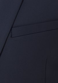 Tessuto di giacca blu navy con una texture liscia, caratterizzato da un design su misura e una tasca sul petto, cucita con precisione sui bordi.