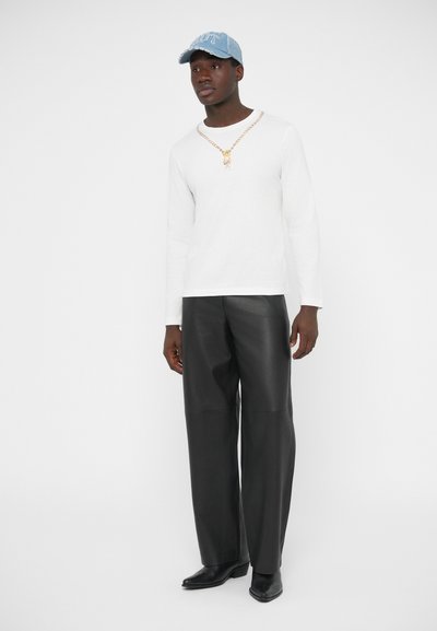 Biele tričko s dlhým rukávom, čierne široké nohavice z umelého koženého materiálu, zlatý náhrdelník retiazkového typu a svetlomodrá rifľová čiapka s nápisom "OUT" v bielom písme.