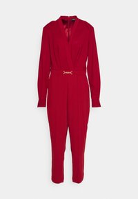 Mono rojo con mangas largas, escote en V, cintura ajustada y un cinturón en tono dorado que acentúa la cintura. Tela suave y ajustada, diseño de pierna recta.