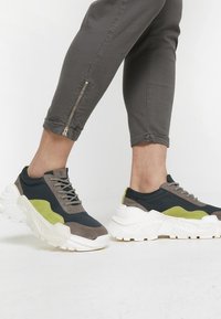 Sportiga sneakers med en kombination av mörkblå mesh, grå mocka och limegröna accenter, med en tjock vit sula och strukturerad design.