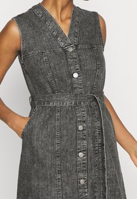Denim dress in dark gray with a button-up front, v-neckline, and belted waist; features side pockets and contrast stitching.