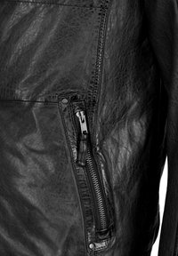 Zwarte leren jas met een gestructureerde afwerking, voorzien van een ritsvak op de mouw, versterkte stiksels en een getailleerd ontwerp.