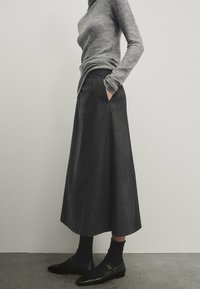 Maglione grigio aderente con maniche lunghe abbinato a una gonna A-line grigio scuro a lunghezza ginocchio, con tasche laterali e scarpe basse nere.