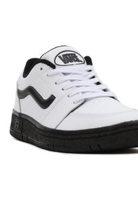 Baskets basses Vans blanches et noires avec semelle noire et bande latérale, lacets blancs et logo Vans sur la languette et la semelle.