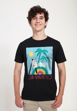 Ung mand smiler, iført en sort t-shirt med sovende Snoopy på en farverig skive, palmer, sol og teksten "Club Paradiso".