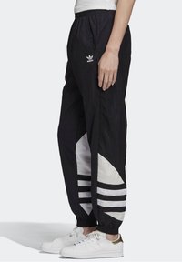 Svarta träningbyxor med en vit geometrisk accent och tre svarta ränder. Tillverkade av lättviktigt material med ett elastiskt midjeband.