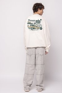 Κρεμ φούτερ με γραφική εκτύπωση ενός αυτοκινήτου και πινακίδων στην πλάτη, σε συνδυασμό με ανοιχτό γκρι φαρδιά παντελόνια με ραμμένα μοτίβα.