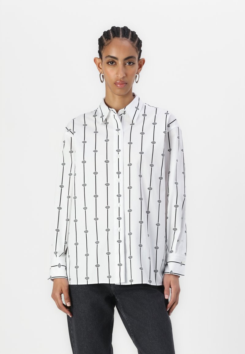 Chemise blanche à boutons avec des rayures noires verticales et un motif répétitif de petites formes ovales. Manches longues avec poignets à bouton.