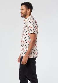 Camicia a maniche corte in tessuto crema con motivi astratti rossi e neri. Presenta un colletto a camicia e una vestibilità comoda.