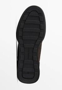 Scarpa in suede marrone con una suola in gomma nera texturizzata, dotata di scanalature orizzontali per la trazione, con un marchio impressi sulla suola.