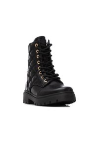 Bota de combate negra con detalles acolchados, ojales dorados, puntera redonda y suela gruesa negra. Presenta cordones y acentos decorativos de hardware.