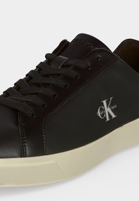 Μαύρο αθλητικό παπούτσι Calvin Klein με μαύρα κορδόνια και λευκή σόλα, με το λογότυπο CK στο πλάι και τη σήμανση στη γλώσσα.