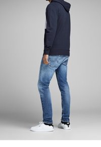 Felpa con cappuccio blu navy abbinata a jeans azzurri chiari. Sneakers bianche con dettagli neri. Cuciture visibili e vestibilità rilassata.