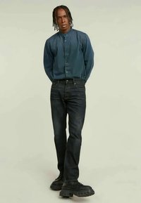 Tumedast sinisest kangast särk, millel on ümar kaelus, kombineeritud kitsaste tumedate teksade ja massiivsete mustade kingadega. Sile kangas ja voolujooneline disain.