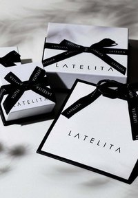 Three gift boxes in white with black accents, featuring black ribbons and the "LATELITA" logo on each box. Varying sizes are displayed.