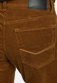 Bruine corduroy broeken hebben een kenmerkende ribbelstructuur, een vijf-pocket ontwerp en een zwarte leren patch met de merknaam op de taille.