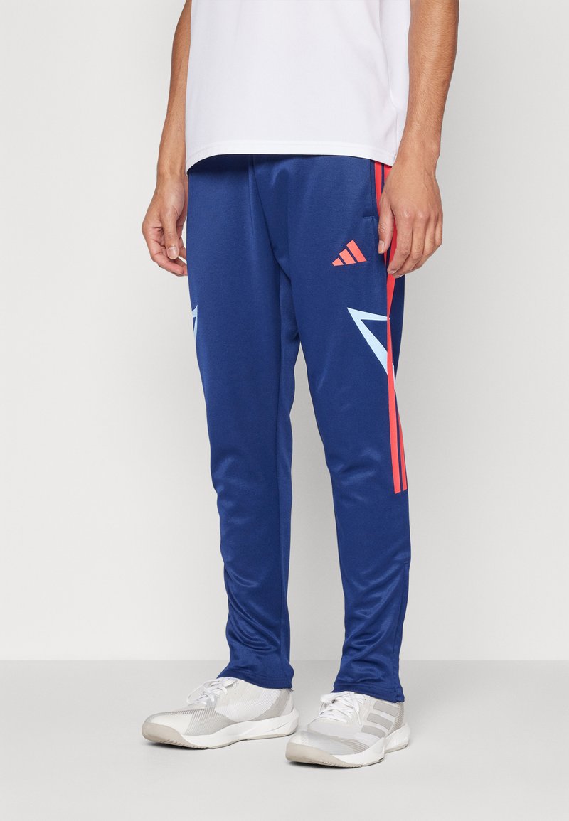 Plave sportske hlače s crvenim i svijetloplavim naglascima, sa vzorcem chevron i Adidas logotipom. Napravljene su od glatkog, laganog materijala.