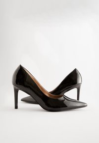 Zwarte hoge hakken van lakleer met spitse neuzen en een gestroomlijnd ontwerp. De hakken zijn ongeveer 10 cm hoog en hebben een gladde afwerking.