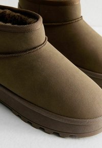 Brązowe botki do kostki wykonane z zamszu, z miękką podszewką, okrągłym noskiem i teksturowaną podeszwą zapewniającą przyczepność.