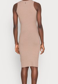 Robe ajustée sans manches en maille côtelée de couleur beige clair, longueur aux genoux avec un col rond, présentant une texture lisse.