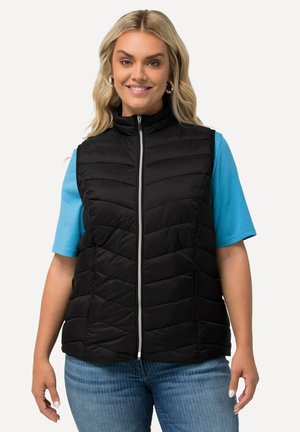 Gilet isolato nero con colletto alto e dettagli a zigzag, abbinato a una maglietta blu e jeans di denim. Chiusura frontale con zip.