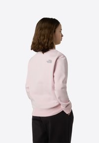 Jasnoróżowa bluza z prążkowanymi mankietami i dołem, z małym szarym logo na plecach. Gładka tkanina z bawełnianej mieszanki i luźny krój.