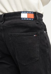 Μαύρο τζιν από τζιν ύφασμα με μπλε και κόκκινο πατζάκι λογότυπου "TOMMY JEANS" στη μέση και μικρή λεπτομέρεια λογότυπου στην πίσω τσέπη.