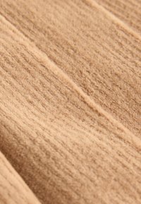 Tissu beige avec une surface douce et texturée, présentant des lignes verticales et de subtiles variations de teinte sur l'ensemble du matériau.