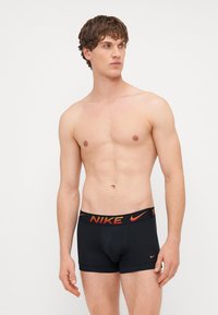 Boxeri negri din material moale, cu un design ajustat; prezintă un logo Nike portocaliu contrastant pe talie.