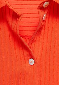 Ljus orange skjorta med en texturerad tyg och vertikala ränder, krage och runda vita knappar.