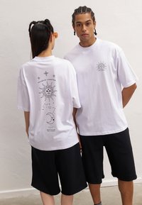 White oversized t-shirts featuring a sun graphic and text on the back, paired with black shorts. Soft cotton material with a casual fit.