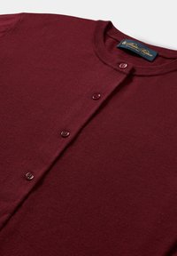 Bordowy swetrowy kardigan z okrągłym dekoltem i czterema pasującymi guzikami z przodu, z widoczną metką wewnątrz kołnierza.