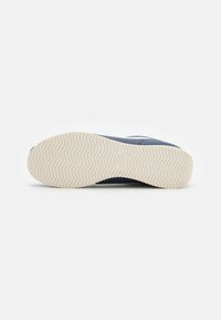 Navy sneaker with a textured fabric upper and a rubber sole featuring a herringbone tread pattern. White accents near the heel.