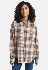 Geknoopte plaid overhemd in wit, bruin en oranje tinten. Het heeft lange mouwen, een kraag en een relaxte pasvorm met een enkele borstzak.