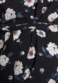 Tecido preto com estampa floral, apresentando flores brancas e cor-de-rosa, complementadas por folhas verdes. Inclui um detalhe de cintura amarrada e pregas.