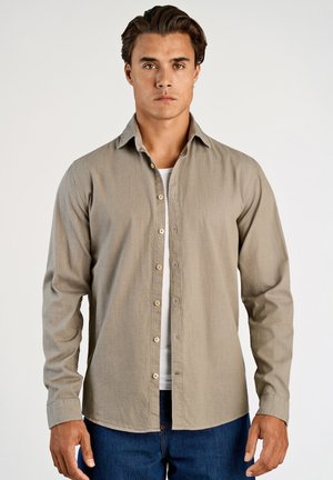 Lichtgrijs overhemd met knopen, een kraag, lange mouwen en een subtiele structuur. Voorzien van bruine knopen en gedragen over een wit ondershirt.