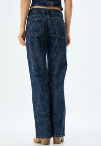Jeans in denim a gamba larga di colore blu scuro con motivo paisley. Presentano una vita alta e tasche posteriori. Tessuto morbido e stile classico.