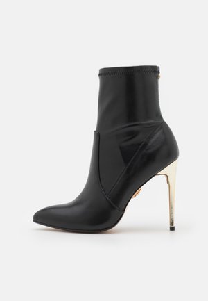Bottine en cuir noir avec un bout pointu et un talon aiguille haut doré. Présente une texture lisse et des détails cousus sur le dessus.