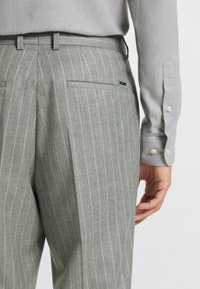 Grårandiga byxor med rak framtill, sidofickor och smal passform. Det strukturerade tyget har en subtil lyster, kompletterad av en ljusgrå skjorta.