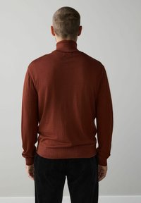 Barna garbó pulóver puha, texturált anyagból, hosszú ujjakkal és testhezálló szabással. Fekete kordbársony nadrággal párosítva.