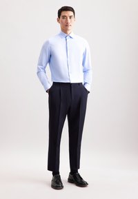 Camicia button-up azzurro chiaro con maniche lunghe abbinata a pantaloni eleganti blu scuro e scarpe da cerimonia nere. Design semplice e pulito.