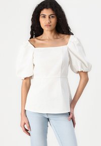 Top alb cu maneci pufoase, decolteu pătrat, corset ajustat și textură de material neted, asortat cu blugi bleu deschis.