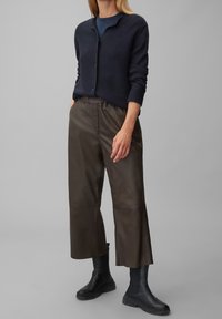 Marinblå stickad cardigan med hög krage, i kombination med bruna läderbyxor i cropped-modell och svarta ankelboots med strukturerade sulor.